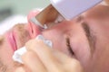 Cosmetologist makes ultrasonic face cleaning procedure to young man in clinic. Royalty Free Stock Photo