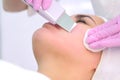 Cosmetologist makes ultrasonic face cleaning procedure to young woman in clinic. Royalty Free Stock Photo