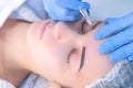 Cosmetologist making eyebrows microblading procedure in beauty salon for girl.