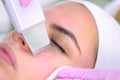 Cosmetologist makes ultrasonic face cleaning procedure to young woman in clinic. Royalty Free Stock Photo