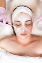 Cosmetologist in medical gloves holds a bowl with cosmetics, applying a brush mask on the client& x27;s face. Top view.Vertical