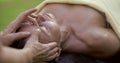 Cosmetologist is performing face massage for adult woman lying on couch in open air, detail view