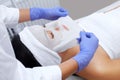 The cosmetologist for procedure of cleansing and moisturizing the skin, applying a sheet mask to the face of a young woman in beau