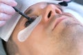 Cosmetologist puts black paint on man& x27;s lashes laminating eyelashes procedure.