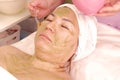 Cosmetologist puts a green mask of fruit kiwi with bones on the female face. Asian woman takes Spa treatments at the beauty salon Royalty Free Stock Photo