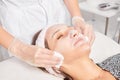 Cosmetologist removing facial cream mask from woman face skin with cosmetic wipes in beauty salon