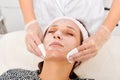 Cosmetologist removing facial cream mask from woman face skin with cosmetic wipes in beauty salon