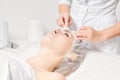 Cosmetologist removing facial cream mask from woman face skin with cosmetic wipes in beauty salon