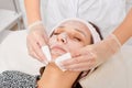 Cosmetologist removing facial cream mask from woman face skin with cosmetic wipes in beauty salon