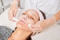 Cosmetologist removing facial cream mask from woman face skin with cosmetic wipes in beauty salon