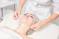 Cosmetologist removing facial cream mask from woman face skin with cosmetic wipes in beauty salon