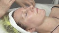 Cosmetologist smear humidify oil on adult woman face by hands in beauty saloon.