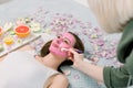 Cosmetologist smears cosmetic facial mask on the face of the pretty young woman in the spa salon. Face mask, spa beauty