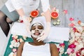 Cosmetologist smears cosmetic mask on the face of the African woman in the spa salon