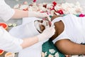 Cosmetologist smears cosmetic mask on the face of the African woman in the spa salon