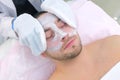 Cosmetologist wipes moisturizing mask from man`s face using terry mittens.