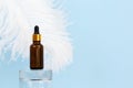 Cosmetology product for facial care. Serum in glass bottle with pipette on glass podium and large white ostrich feather on blue