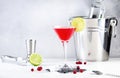 Cosmopolitan alcoholic cocktail drink with vodka, liqueur, cranberry juice, lime and ice. Gray table background, steel bar tools