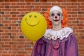 Cosplay: A guy dressed as an evil scary clown similar to Pennywise. A young man as IT against a brick wall with a yellow ball in