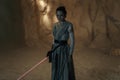 Cosplayer girl portrays character Rey Skywalker from the Star Wars universe with lightsaber in her hand among sandy canyon