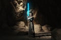 Cosplayer girl portrays character Rey Skywalker from the Star Wars universe with lightsaber in her hand among sandy canyon