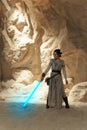 Cosplayer girl portrays character Rey Skywalker from the Star Wars universe with lightsaber in her hand among sandy canyon