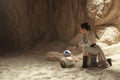 Cosplayer girl portrays character Rey Skywalker from the Star Wars universe sitting near astromechanical droid BB-8 among sandy