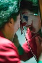 Cosplayer in the image of the crazy clown laughs in front of a broken mirror