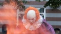 A cosplayer with makeup and a costume like a scary clown Pennywise appears from the fire in the background of a building