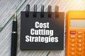 COST CUTTING STRATEGIES text with fountain pen, calculator and notepad on wooden background