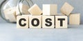 Cost, expense or company profit and loss concept, cube wooden block with alphabet combine word COST on white grid paper Royalty Free Stock Photo