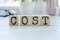 Cost, expense or company profit and loss concept, cube wooden blocks with alphabet combine word COST on office desk