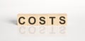 COSTS word from wooden blocks on the white desk