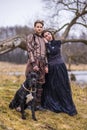 Costume Play. Couple as Knight Warrior and Princess with Black Dog Posing in Medieval Clothing in Spring Forest Outdoors