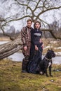 Costume Play Project. Couple as Knight Warrior and Princess with Black Dog Posing in Medieval Clothing in Spring Forest Outdoors