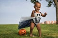 Costumed baby taking his first steps on the grass playing to put candy into a pumpkin in an outdoor park, celebrating halloween. Royalty Free Stock Photo