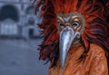 Costumed carnival-goer with red feathered mask standing in St Mark`s Square during Venice Carnival Carnivale di Venezia.