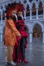 Costumed carnival-goers with red feathered mask standing in St Mark`s Square during Venice Carnival Carnivale di Venezia.