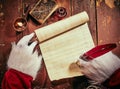 Costumed hands of Santa Claus writing a Christmas letter or greeting on a blank parchment scroll by candlelight on a vintage Royalty Free Stock Photo