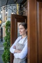 Smiling cute waitress leaning on door with her arms crossed