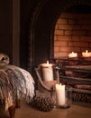 Cosy tartan blanket near fire place with lit candles and pinecones Royalty Free Stock Photo