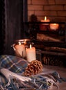 Cosy tartan blanket near fire place with lit candles and pinecones Royalty Free Stock Photo