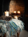 Cosy tartan blanket near fire place with lit candles and pinecones Royalty Free Stock Photo