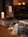Cosy tartan blanket near fire place with lit candles and pinecone