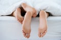 Cosy under the covers. Cropped image of a couples bare feet sticking out from under the duvet while lying in bed. Royalty Free Stock Photo