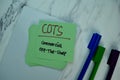 COTS- Commercial Off-The-Shelf write on sticky note isolated on Wooden Table. Business Concept