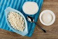 Cottage cheese in blue bowl, sour cream in bowl, spoon on napkin, sugar in white bowl on table. Top view