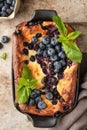 Cottage cheese casserole with blueberries and mint leaves deciration in baking dish on brown rustic textured background