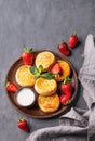 Cottage cheese, cheesecakes or syrniki with sour cream, strawberries and mint leaves on a wooden plate on a dark background with