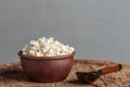 cottage cheese in a clay plate on a gray background, a wooden spoon on an old wooden table